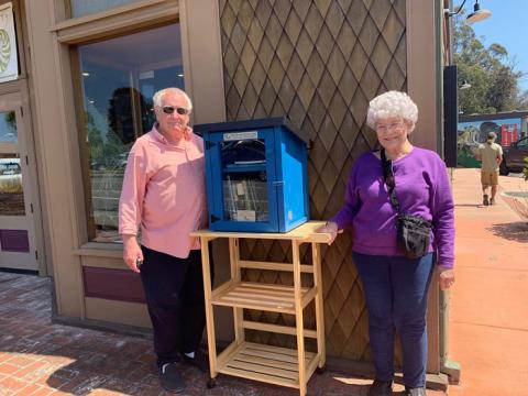 Philip and Manette Gerstle posing next to the little free library stand out in front of the Museum